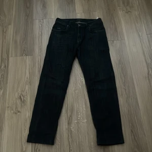 Svarta jeans från Emporio Armani - Snygga svarta jeans från Emporio Armani med diskret tvättad look. Klassisk femficksmodell med silverfärgad logga på fickan fram och bak samt svart patch med logotyp i midjan. Jeansen har raka ben och normal passform, perfekta för en stilren vardagslook.