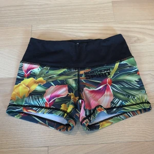 tränings shorts Northern Spirit - Färgglada träningstights-shorts från Northern Spirit med tropiskt blommönster i gult, rosa, orange och grönt. Hög midja i svart och tight passform, perfekta för gymmet