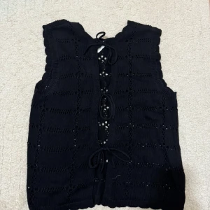 Svart stickad väst/koftafrån Object - VeroModa - Svart stickad väst från Object med snyggt hålmönster och knytband framtill. Köpt på VeroModa aldrig använd. Perfekt att slänga över en t-shirt eller skjorta för en lager-på-lager-look. Perfekt till hösten 😍