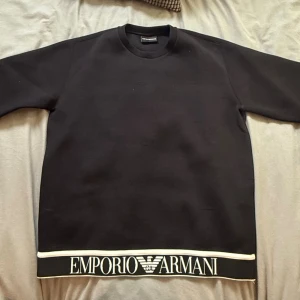 Svart sweatshirt Emporio Armani M - Svart sweatshirt från Emporio Armani i storlek M. Tröjan har rund halsringning, långa ärmar och en bred vit logotypdetalj längs nederkanten. Tillverkad i mjuk bomullsmix för en clean och stilren look.        Pris kan diskuteras vid snabb affär 😁