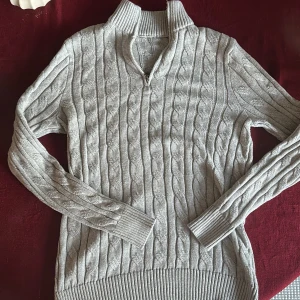 Ljusgrå kabelstickad half zip tröja - Snygg ljusgrå kabelstickad tröja med half zip och hög krage. Den är aldrig använd då den är lite för liten på mig och det gick ej att returnera varan. Ny pris ca 800kr. Jag som bär på bilden är ca 190cm lång. Varan är i storlek M.
