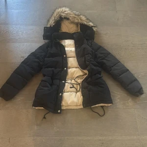 Ralph Lauren - Svart pufferjacka från Denim & Supply Ralph Lauren med beige insida och huva med fejkpäls. Jackan har snörning i midjan, dragkedja och tryckknappar framtill. Perfekt för kalla dagar med sin tjocka vaddering och långa ärmar. Vänstersidan fram lite solblekt( Kanske inte men jag ser det haha) därav priset men syns knappt. Superfin❤️ Endast swish betalning skickas spårbart 59kr annars mötas❤️