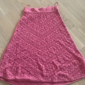 Rosa stickad långkjol från Indiska - Supersöt rosa midikjol från Indiska i stickad bomull med snyggt hålmönster och bred resår i midjan. Kjolen har en lätt utsvängd form och känns både luftig och trendig. Perfekt för dig som gillar färg och vill ha något unikt i garderoben.