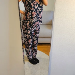 Blommigt set med linne och byxor - Supergulligt set med linnetopp med smala axelband och byxor från Zoul Edition i storlek XS. Toppen är svart med ett blommigt mönster i rosa och vitt, har v-ringad hals och ärmlös design. Kan användas tillsammans eller separat. Bara använda några få gånger