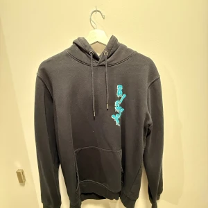 Risky hoodie - Svart hoodie från Risky med blått tryck på bröstet. Perfekt för dig som gillar streetwear och vill ha en chill look. Jag säljer då stilen inte riktigt passar mig och tröjan är använd väldigt få gånger