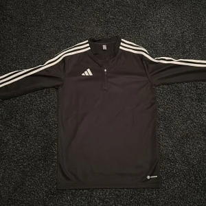 Svart Adidas half zip tröja och byxor  - Svart långärmad Adidas-tröja med vita ränder längs ärmarna och klassisk logga på bröstet. Tröjan har half zip och är tillverkad i lätt polyester med AEROREADY-teknologi, perfekt för träning eller sportiga outfits. Jag köpte den i xxl och jag har bara använt den två gånger. Ochså de ingår adidas byxor!
