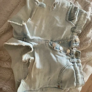 Ljusblåa jeansshorts  - Säljer ett par ljusblåa jeansshorts från zara. Shortsen har flera slitningar och knappar framtill, samt stora bakfickor. Perfekta för en avslappnad och trendig look i sommar.