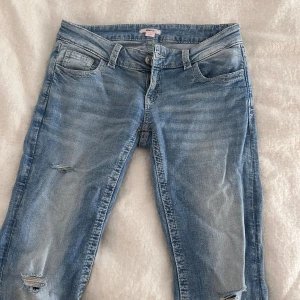 Slutsålda - Blå lågmidjade jeans med broderade bakfickor - Snygga ljusblå lågmidjade jeans från Gina Tricot som är helt slutsålda med slitningar på benen och broderade detaljer på bakfickorna. Klassisk femficksmodell med knapp och dragkedja framtill. Perfekta för en avslappnad och trendig look.