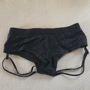 Svart bikiniunderdel från Polerina - Svart underdel från Polerina med bred midja och coola dubbla sidoband. Tillverkad i 100% polyester som känns mjuk och följsam mot huden. Snygg och enkel design. Aldrig använda.