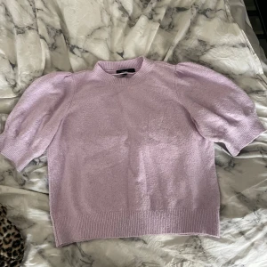 Ljuslila stickad topp med puffärm - Superfin ljuslila stickad topp från Gina Tricot med korta puffärmar och ribbade kanter. Perfekt för dig som vill ha en söt och trendig look med lite volym på axlarna. Enkel att styla till både jeans och kjol.