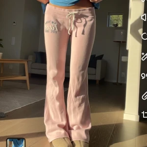Ljusrosa mjukisbyxor med snörning - Säljer ett par ljusrosa mjukisbyxor med bootcut-snitt och snörning i midjan. Byxorna har tryck med text på ena höften och är gjorda i mjukt material, perfekta för chill dagar. Snygg och avslappnad passform.