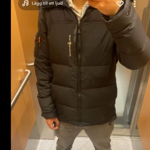 Svart  jacka från sail racing - Säljer en svart jacka från sail racing med dragkedja framtill och logga på bröstet. Jackan har lång ärm, hög krage och en ficka med orange dragkedja på ärmen. Perfekt för kalla dagar och riktigt skön att bära. Fler bilder privat, pris kan diskuteras vid snabb affär