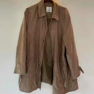 Beige parkajacka från Geico - Stilren beige parkajacka från Geico med klassisk krage och dragkedja framtill. Jackan har långa ärmar, fickor med dragkedja och knappar vid ärmsluten. Perfekt för dig som gillar en enkel och clean look.