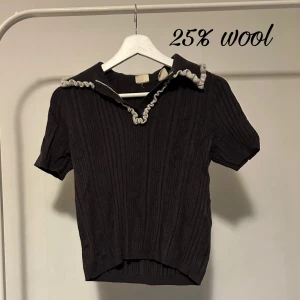 Svart ribbad Levi's pikétröja med krage - Svart ribbad pikétröja från Levi's med korta ärmar och kontrastfärgad volangdetalj längs kragen. Tröjan har en klassisk pikékrage och är tillverkad av 25% ull, 45% polyamid och 30% viskos. Perfekt för dig som gillar en stilren look med twist.