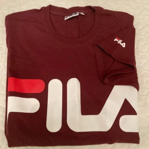 Vinröd FILA t-shirt med stor logga - Säljer en vinröd t-shirt från FILA i storlek S. T-shirten har en stor vit och röd FILA-logga framtill och en mindre logga på ärmen. Klassisk rund hals och korta ärmar. Tillverkad i mjuk bomull som är skön att ha på sig.