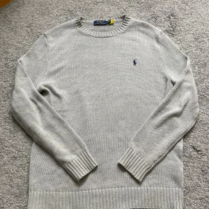 Grå stickad tröja från Polo Ralph Lauren - Snygg grå stickad tröja från Polo Ralph Lauren med klassisk rund hals och broderad marinblå logga på bröstet. Tröjan är sparsamt andvänd. Vid frågor bara hör av dig så svarar jag gärna. Priset är förhandlingsbart!