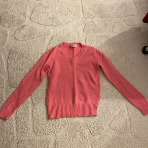 Rosa v-ringad tröja från Boomerang - Säljer en rosa v-ringad tröja från Boomerang i storlek XS. Tröjan har långa ärmar, ribbade muddar och nederkant samt en klassisk passform. Perfekt för dig som gillar stilrena och färgglada plagg.