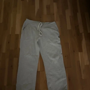 Grå mjukisbyxor från Polo Ralph Lauren - Snygga ljusgrå mjukisbyxor från Polo Ralph Lauren med klassisk broderad logga på benet. Byxorna har dragsko i midjan och är tillverkade i mjuk bomullsmix för extra komfort. Perfekta för chill dagar eller när du vill vara bekväm men ändå se fräsch ut.
