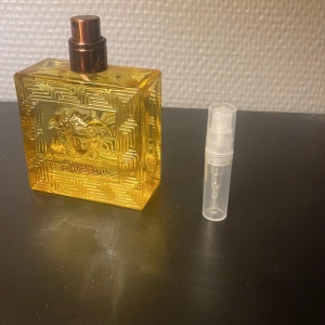 Versace Eau de Parfum flaska - Snygg Versace Eau de Parfum i guldig flaska med ikonisk Medusa-detalj. Perfekt för dig som vill sticka ut och addera lite lyx till din stil. Levereras med en praktisk liten sprayflaska för enkel påfyllning och användning.
