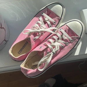 Rosa Converse sneakers låga - Säljer ett par klassiska Converse sneakers i en snygg rosa färg med vita snören och tåhätta. Skorna är låga och har en platt sula, tillverkade i canvas med gummidetaljer. Perfekta för dig som vill ha en poppig färg på fötterna. Lite slitningar inne i skorna, men inget som påverkar!💕