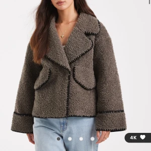 Grå teddyjacka med svarta detaljer - Mysig grå teddyjacka med markerade svarta sömmar och bred krage. Jackan har två fickor framtill och en boxig, loose passform. Perfekt för dig som gillar en trendig och avslappnad stil.