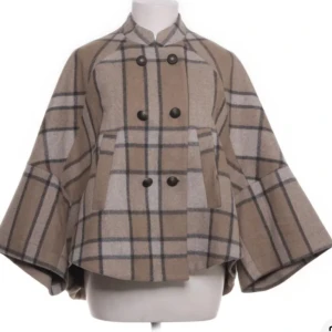 Rutig kappa i ullmix med vida ärmar - Snygg rutig kappa i beige och grå toner med breda, vida ärmar och dubbelknäppning framtill. Jackan har en klassisk krage och stora fickor, perfekt för dig som vill sticka ut med en trendig och mysig look.