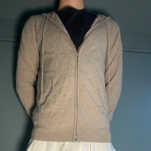 Beige hoodie i kashmir från John Henric - Använd 6-7 gånger, Priset ej hugget i sten. Nypris 2499kr! Mjuk och lyxig beige hoodie från John Henric i kashmir. Tröjan har huva, dragkedja framtill och två fickor. Perfekt för dig som gillar chill och stilren look. Långärmad och med ribbade muddar för extra komfort.