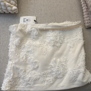 Vit blommig topp från BikBok - Supersöt vit topp från BikBok med 3D-blommor och broderade detaljer. Toppen har en figurnära passform och är gjord i polyester. Perfekt för dig som vill sticka ut med en romantisk vibe.