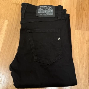Svarta Replay Anbass jeans, stl 30/32 - Svarta Replay Anbass jeans i slim fit med klassisk femficksdesign. Byxorna har raka ben, diskret logga på bakfickan och är tillverkade i stretchigt bomullsmaterial för skön passform. Perfekta för dig som gillar stilrena och snygga jeans. Jeansen är i bra skick köpt på Zalando för 900kr pris 349kr men kan diskuteras vid snabb affär 