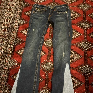 True Religion mörkblå jeans med kontrastsöm - Säljer ett par mörkblå jeans från True Religion med tydliga kontrastsömmar i orange och vit. Klassisk femficksmodell med snygga detaljer på bakfickorna och logopatch. Jeansen har raka ben och är tillverkade i slitstarkt denim.