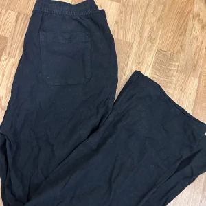 Svarta linnebyxor med snörning, S - Svarta linnebyxor i storlek S med elastisk midja och snörning framtill. Byxorna har sidfickor och en bakficka, rak passform. Luftigt material som passar skönt när det är varmt.