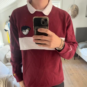 Golftröja Lyle & Scott x Malbon - Vinröd pikétröja från Lyle & Scott x Malbon med vit krage. Perfekt för höstgolfen.