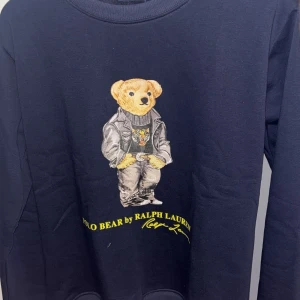 Mörkblå sweatshirt Polo Bear Ralph Lauren - Säljer en mörkblå sweatshirt från Ralph Lauren med ikoniska Polo Bear-trycket framtill. Tröjan har rund halsringning och långa ärmar. Perfekt för dig som gillar streetstyle och vill ha något unikt i garderoben. Varan är självklart äkta
