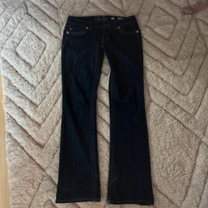 Miss Me bootcut jeans - Mörkblå bootcut jeans från Miss Me med snygga broderade bakfickor dekorerade med bling och mönster. Klassisk femficksmodell med silverfärgade detaljer och kontrastsömmar. Perfekta för dig som vill sticka ut lite extra. Lite slitna längst ner på benen, samt en sten som gott bort på bakfickan, annars jättebra skick!⭐️💕MÅTT: midja- 40cm, längd- 108cm💗(fråga om bild på defekter!!)