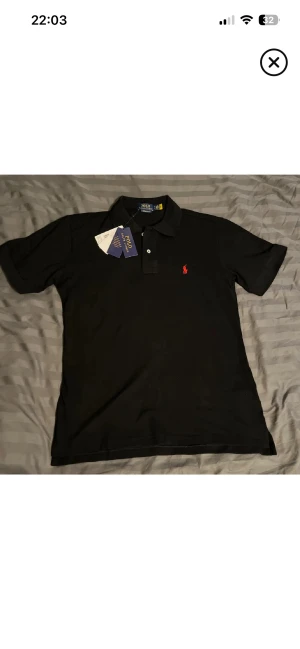 Svart piké från Polo Ralph Lauren - Säljer en helt ny svart pikétröja från Polo Ralph Lauren i bomull med röd broderad logga på bröstet. Slim fit-modell som sitter snyggt och stilrent. Mitt pris 599kr!💥Perfekt julklapp🎄 