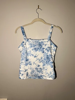 Blommig vit och blå linnetopp - Säljer en söt linnetopp med blommigt mönster i blått och vitt. Toppen har raka axelband och smockad rygg med knytband för extra detalj. Materialet känns lätt och somrigt, perfekt för varma dagar. Köpt second hand och är från märket ”Rihoas” storlek S men passar även mig som har XS🌟💕❤️ 