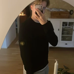 Svart stickad Stone Island tröja - Svart stickad tröja från Stone Island med klassisk rund hals och ikonisk patch på vänster ärm. Tröjan har ribbade muddar och en clean look som är enkel att matcha. Perfekt för dig som gillar streetwear och vill ha något stilrent med edge.