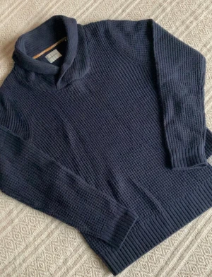 Jack & Jones Stickad Tröja - Snygg mörkblå polotröja från Jack & Jones i grovstickad bomull. Tröjan har lång ärm, ribbade muddar och en bred krage som ger en chill och stilren vibe. Perfekt för dig som gillar klassisk men modern look.
