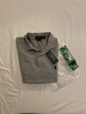 Grå pikétröja från Polo Ralph Lauren - Säljer en jätte snygg piké ifrån Ralph Lauren. Den är i toppen skick med inga skador. Den är lite stor i storleken så passar M. Skriv till mig vid intresse❤️ Obs påsen tillkommer inte 