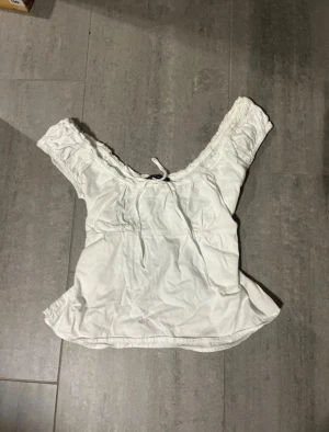 Vit blus med spets från Brandy Melville - Supersöt vit blus från Brandy Melville med spetsdetaljer runt halsringningen och ärmarna. Blusen har korta puffärmar, knytband fram. Tillverkad i bomull🩷