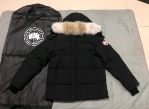 Svart Canada Goose dunjacka med päls - Säljer en svart dunjacka från Canada Goose med avtagbar huva och äkta pälsdetalj. Jackan har klassisk patch på ärmen, stora fickor och quiltad design. Perfekt för kalla vinterdagar och riktigt snygg streetstil.