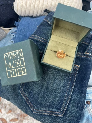Guldring Face från Maria Nilsdotter - Unik guldfärgad ring från Maria Nilsdotter med ett coolt ansikte som motiv. Ringen har en rund form och levereras i originalask. Perfekt för dig som vill sticka ut med ett smycke som har personlighet och edge.
