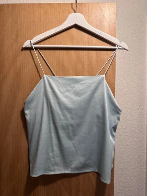 Ljusblå satin linnetopp från Zara - Säljer en ljusblå linnetopp från Zara i satin med tunna axelband och slät, glansig yta. Toppen har en enkel och stilren design.