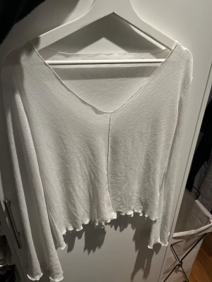 Vit långärmad topp med v-ringning - Säljer en vit långärmad topp med v-ringad hals och  passform. Toppen har vågiga kanter vid ärmslut och nederkant som ger en extra söt touch. Den är lätt genomskinlig.