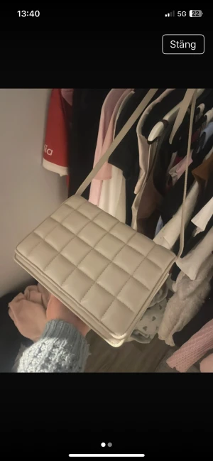 Beige quiltad axelväska med dragkedja - Snygg beige axelväska med quiltad design och rektangulär form. Väskan har ett långt axelband och insidan är ljus med en praktisk ficka med dragkedja. Perfekt för att bära dina essentials och ger en clean vibe till din outfit.