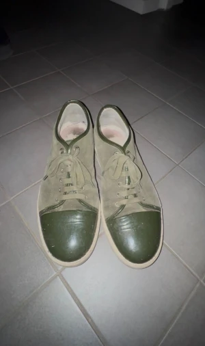 Gröna sneakers från Lanvin i mocka - Snygga gröna sneakers från Lanvin med ovandel i mocka och lackade detaljer på tån och runt öppningen. Skorna har snörning och en platt, vit sula. Perfekt för dig som gillar en clean men ändå unik look.