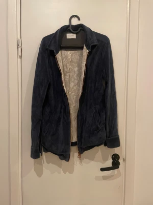 Blå mockajacka från Limitato - Snygg blå mockajacka från Limitato med dragkedja och klassisk krage. Jackan har långa ärmar med knappdetalj vid mudden och ett ljust innerfoder med subtilt mönster. Perfekt för dig som vill ha en stilren och tidlös look.