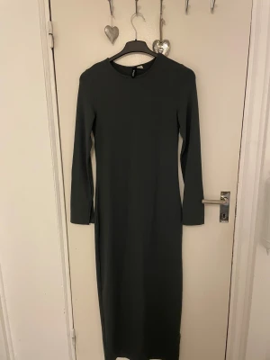 Svart/mörkgrå långärmad klänning H&M Divided - En stilren svart/mörkgrå långklänning från H&M Divided med lång ärm och rund halsringning. Klänningen har en rak passform och är tillverkad i ett mjukt, stretchigt material som sitter snyggt på kroppen. Perfekt för dig som gillar minimalistisk och clean stil. Den har slitsar i armarna och en lång bak som slutar vid knävecket på mig ungefär, jag är 1.60. Har bara använt en gång då jag inte är bekväm i den