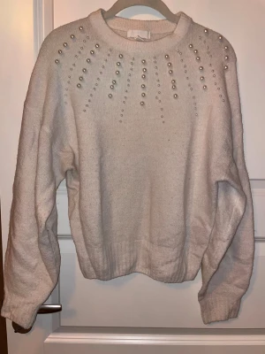 Vit stickad tröja med pärlor från H&M - Superfin vit stickad tröja från H&M med pärldetaljer över axlar och bröst. Rund halsringning och långa ärmar, mjukt material som känns skönt mot huden. Perfekt för dig som gillar att sticka ut med snygga detaljer.