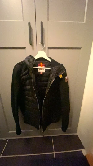Svart cardigan Parajumpers M -  Säljer nu min jacka som jag har använt max 2 gånger och jackan är i helt nytt skick låda och galje följer med. Svart cardigan från Parajumpers med huva och coolt badge på ärmen. Jackan har quiltad framsida och rygg, meshade ärmar och sidor, samt dragkedja fram och bak. Passar även storlek s.